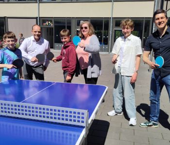 Mehrere Kinder und Erwachsene stehen im Pausenhof an der Tischtennisplatte.