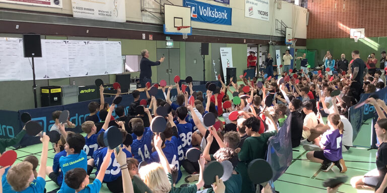 Kinder in der Turnhalle halten ihre Tischtennisschläger in die Luft