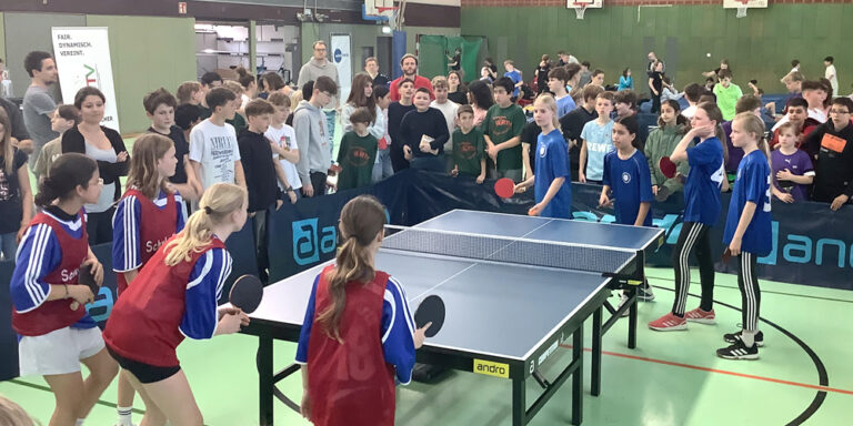 Zwei Mädchenteams spielen Rundlauf an einer Tischtennisplatte. Das eine Team trägt rote Leibchen.