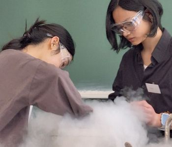 Zwei Mädchen mit Schutzbrillen. Weißer Rauch im Vordergrund.