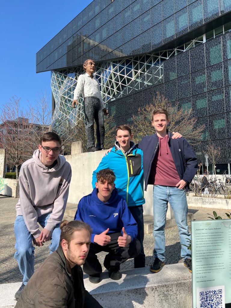 Mehrere Schüler stehen vor einer Statue. Die Sonne scheint.